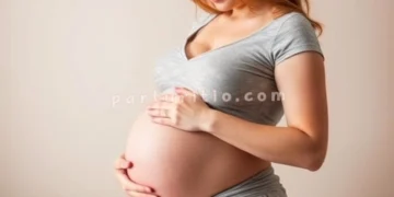 Mujer embarazada sentada en la cama acariciando su vientre.