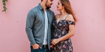 Pareja joven mirándose con complicidad frente a una pared decorada con flores.