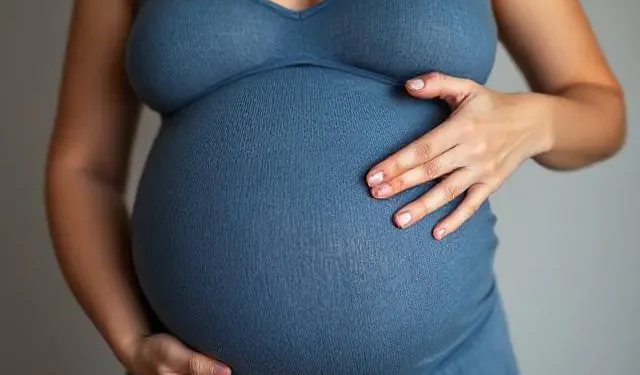 Mujer embarazada con vestido azul tocando su vientre con ambas manos.